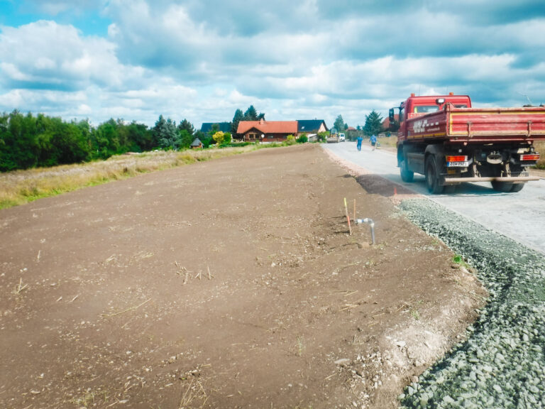 bschluss der Erschließungsarbeiten: Eine planierte Fläche neben einer frisch geschotterten Zufahrt, markiert das Bauende eines Projekts von Geo Service Glauchau. Ein roter LKW ist teilweise sichtbar