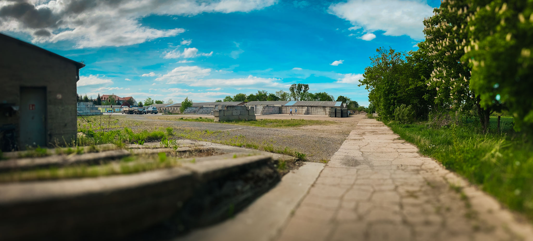Übersicht eines weitläufigen Industriegeländes oder Altstandorts unter blauem Himmel, mit Lagergebäuden und Freiflächen.